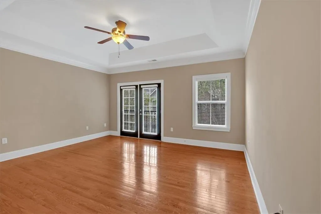 Empty room featuring hardwood / wood-style floors, a raised ceiling, ornamental molding, baseboards, and ceiling fan