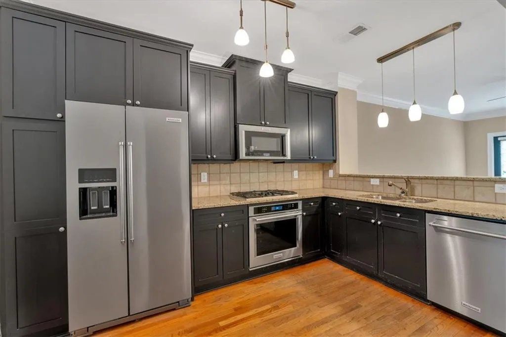 Kitchen with a sink, visible vents, appliances with stainless steel finishes, light stone counters, and ornamental molding