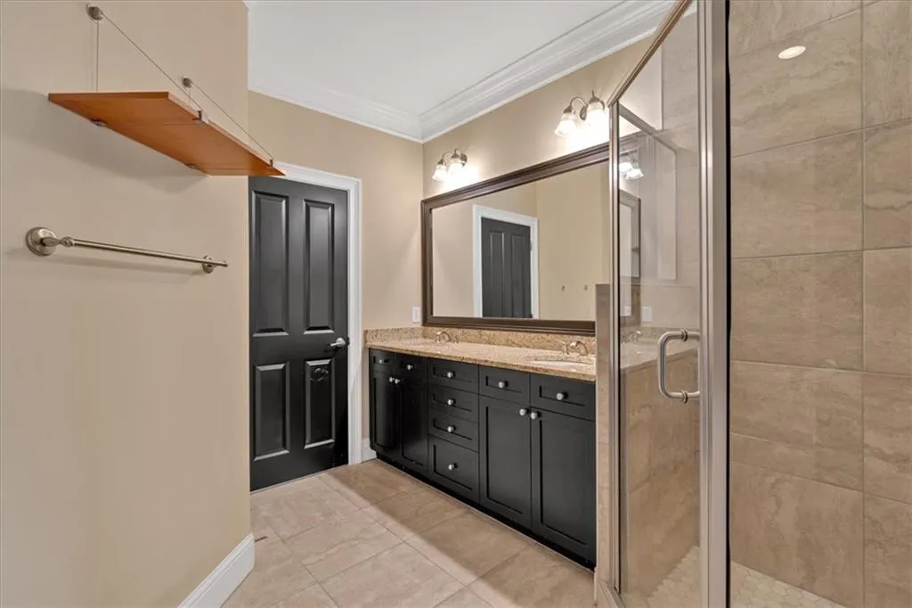 Full bath featuring tile patterned floors, a sink, double vanity, a shower stall, and ornamental molding