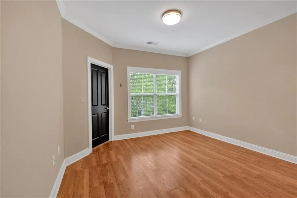 Empty room featuring light wood-type flooring, baseboards, visible vents, and ornamental molding