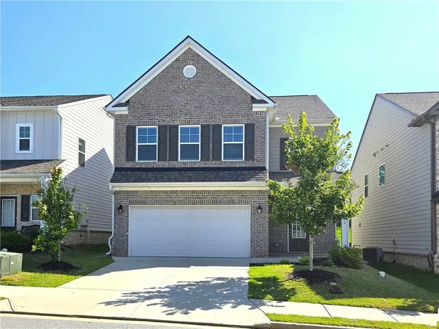 Brick Colonial featuring a gabled roofline with architectural detailing, three upper-level windows with black trim, and a two-car garage with white paneled doors