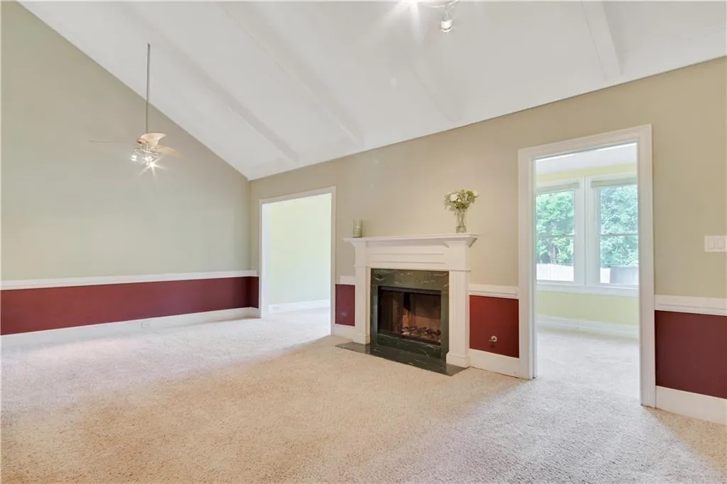 Unfurnished living room featuring beamed ceiling, carpet, a fireplace, baseboards, and ceiling fan