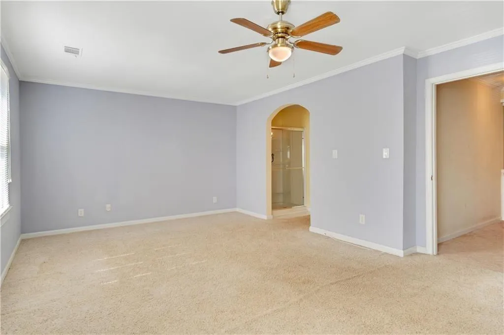 Unfurnished room featuring crown molding, visible vents, arched walkways, and ceiling fan