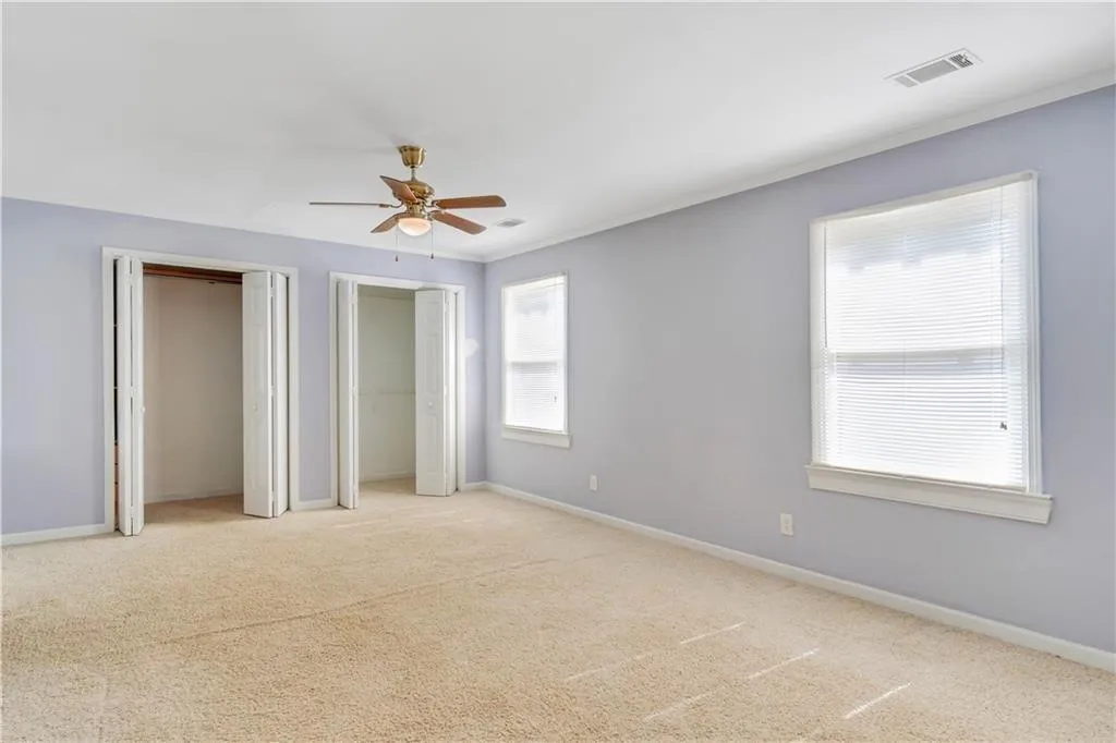 Unfurnished bedroom with light carpet, baseboards, visible vents, and multiple closets