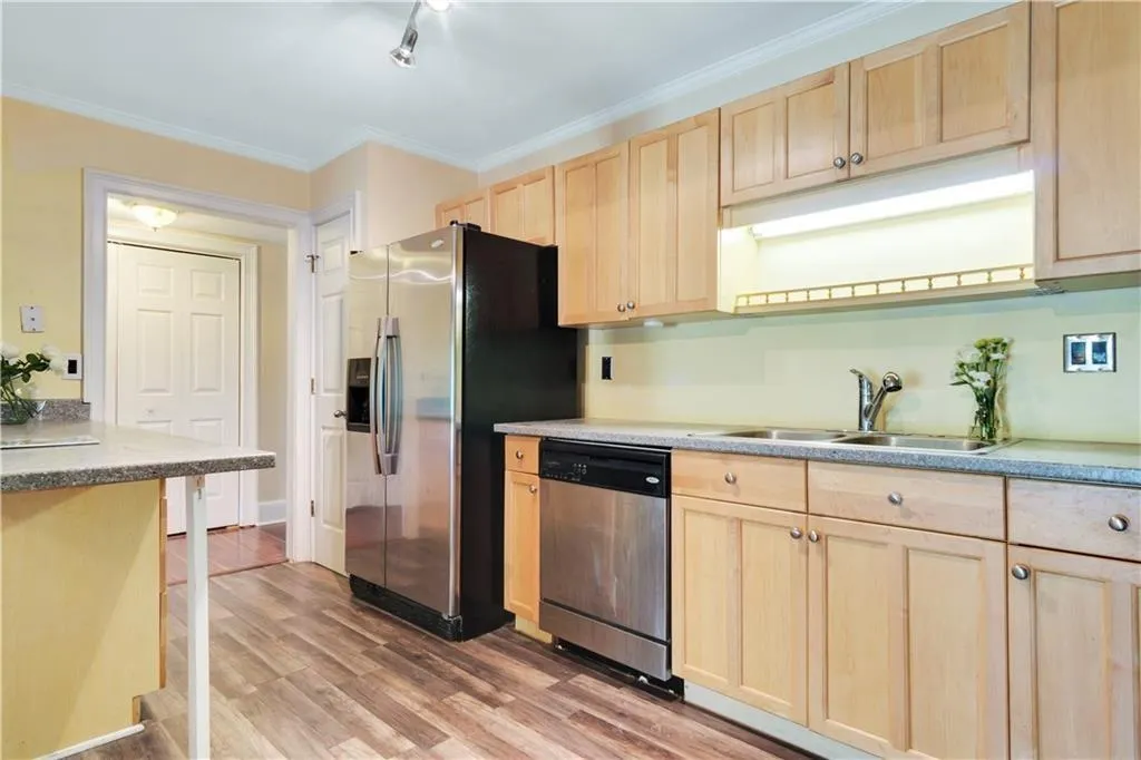 Kitchen with light wood finished floors, light brown cabinetry, ornamental molding, appliances with stainless steel finishes, and a sink