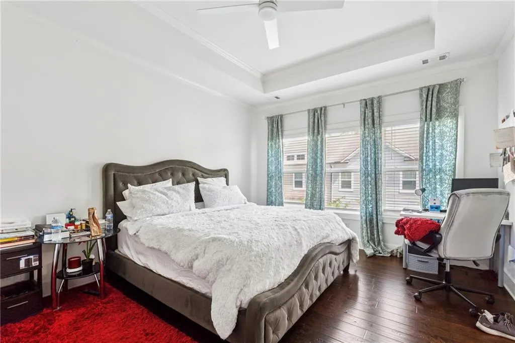 Bedroom with a raised ceiling, crown molding, wood-type flooring, and ceiling fan