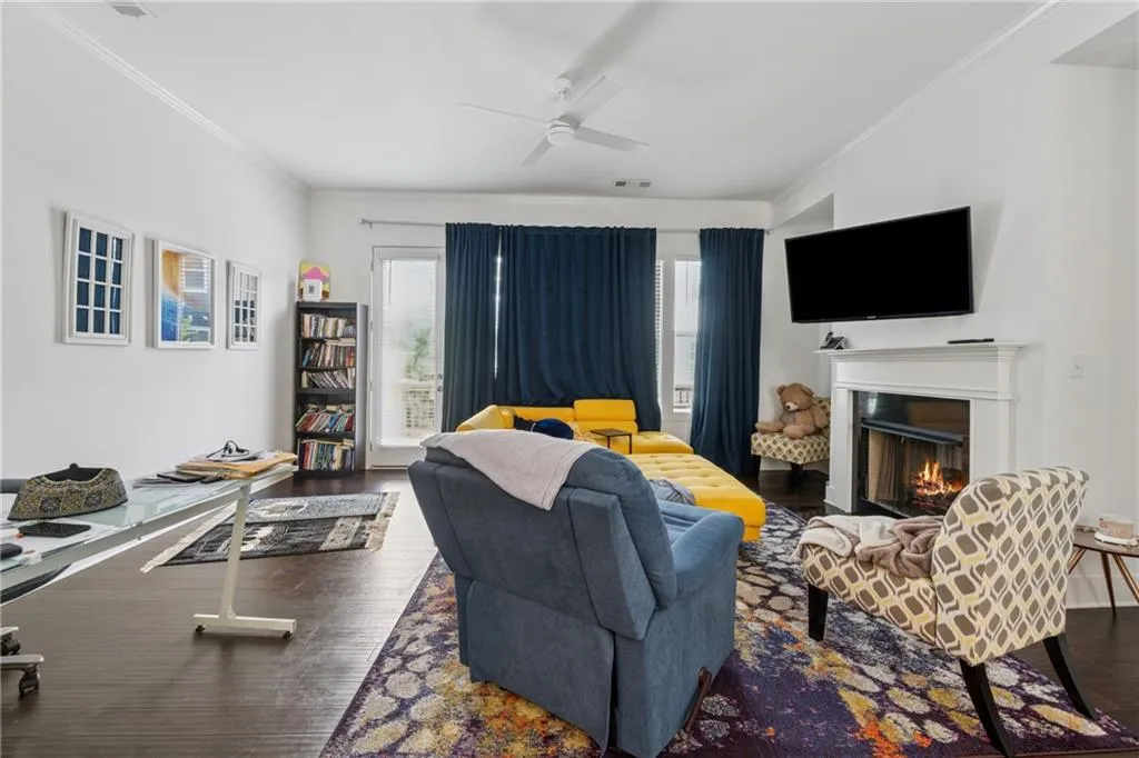 Living area with ceiling fan, crown molding, wood finished floors, and a warm lit fireplace