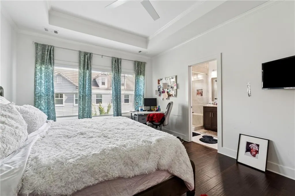 Bedroom with a tray ceiling, dark wood-style flooring, ornamental molding, a ceiling fan, and ensuite bathroom