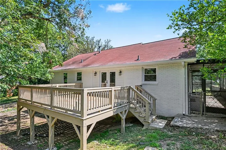 Expansive wood-finish deck with railing and stairs, white brick exterior, red roof shingles, and exterior lighting fixtures