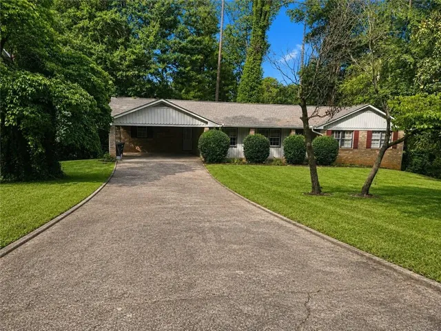Brick ranch home featuring a long asphalt driveway, attached two-car garage, and manicured front lawn with mature landscaping and established trees