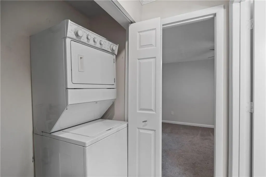 Laundry room with stacked washer / dryer, carpet flooring, and baseboards