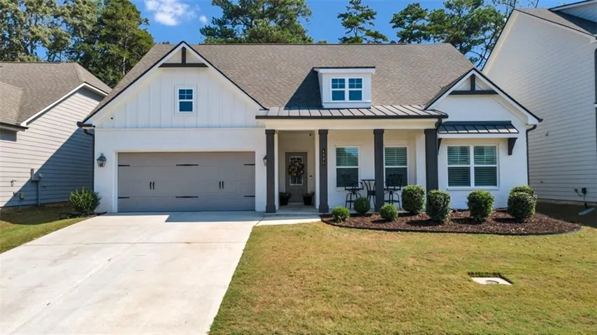 White exterior with dark trim accents, covered entry with columns, gray garage door, dormer window, and mature landscaping