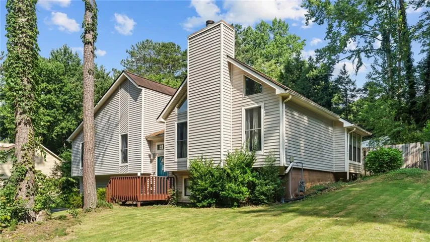 Multi-level dwelling featuring horizontal siding, a prominent chimney, and a wooden deck