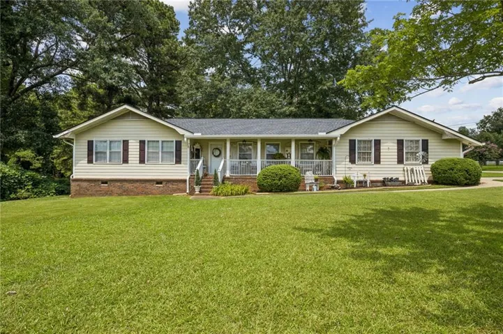 Ranch-style residence featuring a covered front porch with white railings, brick accent foundation, and light-colored siding
