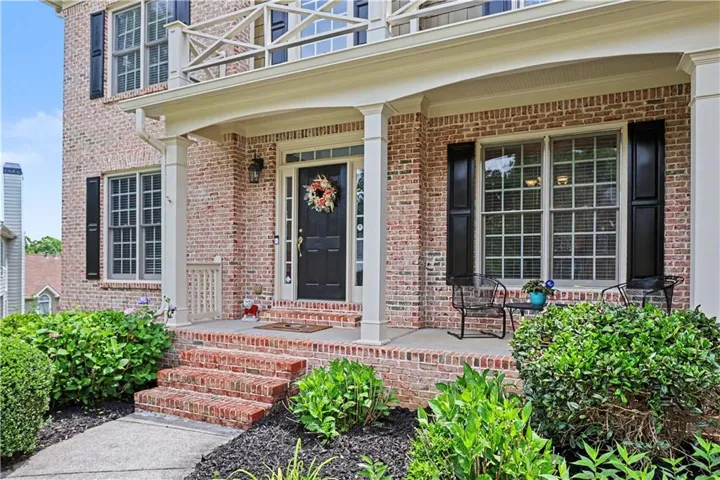 Brick exterior featuring a covered front porch with white columns, brick steps, and multiple paned windows with black shutters