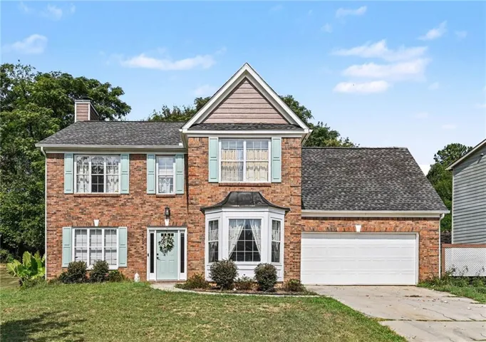Brick exterior featuring a two-car garage, bay window, and gabled roofline with shingle siding accents