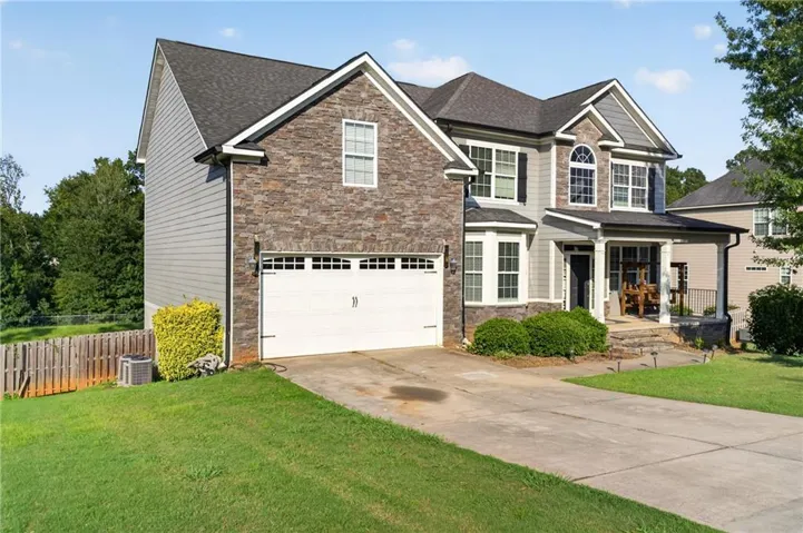 Two-story exterior featuring stone and siding, covered front porch, arched window, attached two-car garage, and a concrete driveway