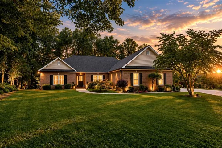 Brick exterior with a dark shingle roof, featuring shuttered windows, a manicured lawn, and mature trees