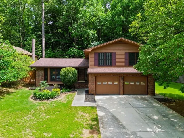 Split-level residence featuring a two-car garage with panel doors, brick accents, and a concrete driveway