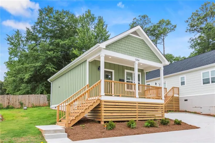 Green exterior siding with white trim and a covered front porch featuring natural wood railings and steps