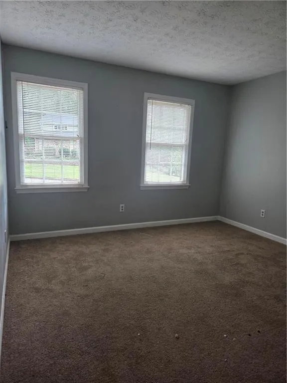 Empty room with a textured ceiling and dark carpet