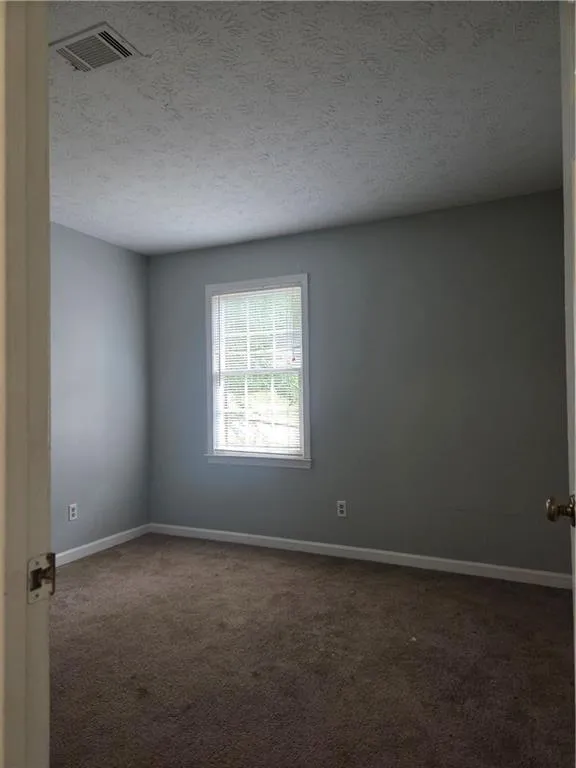 Spare room with a textured ceiling and dark colored carpet