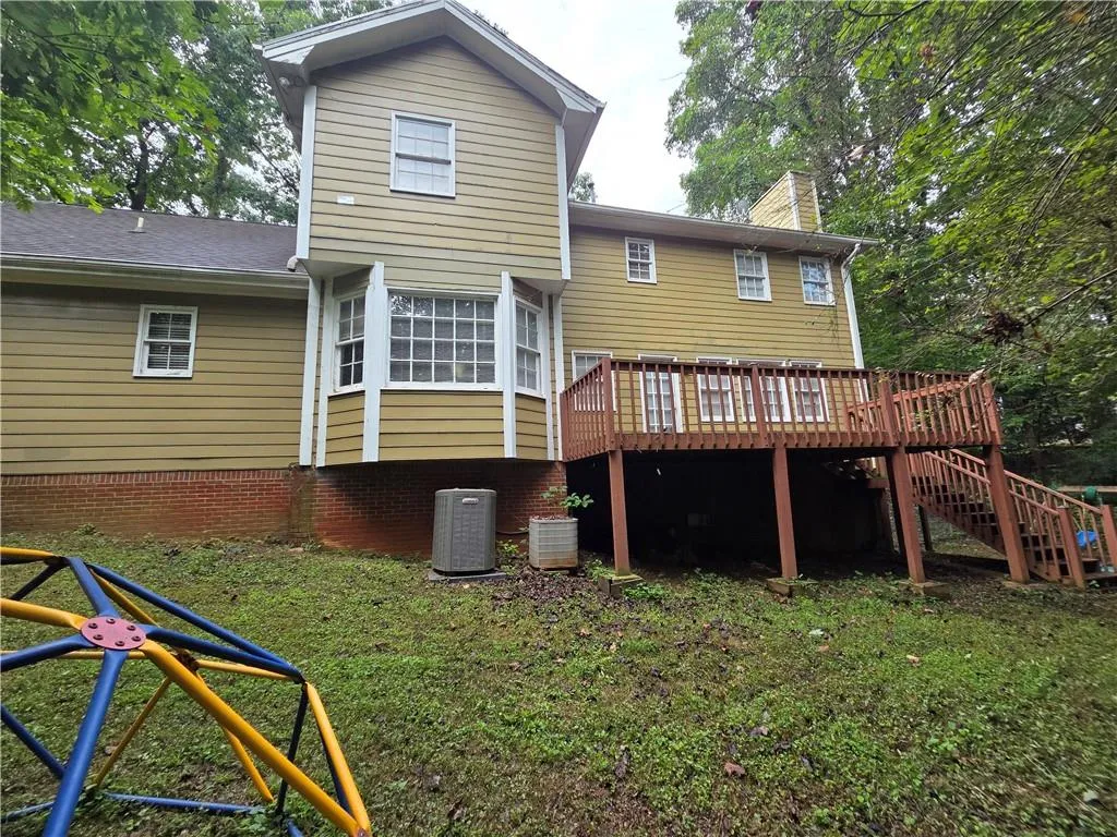 Back of house featuring a wooden deck, stairway, a chimney, and a lawn