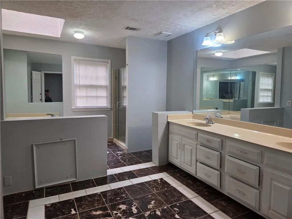 Full bathroom featuring double vanity, a skylight, a stall shower, and dark marble finish floors