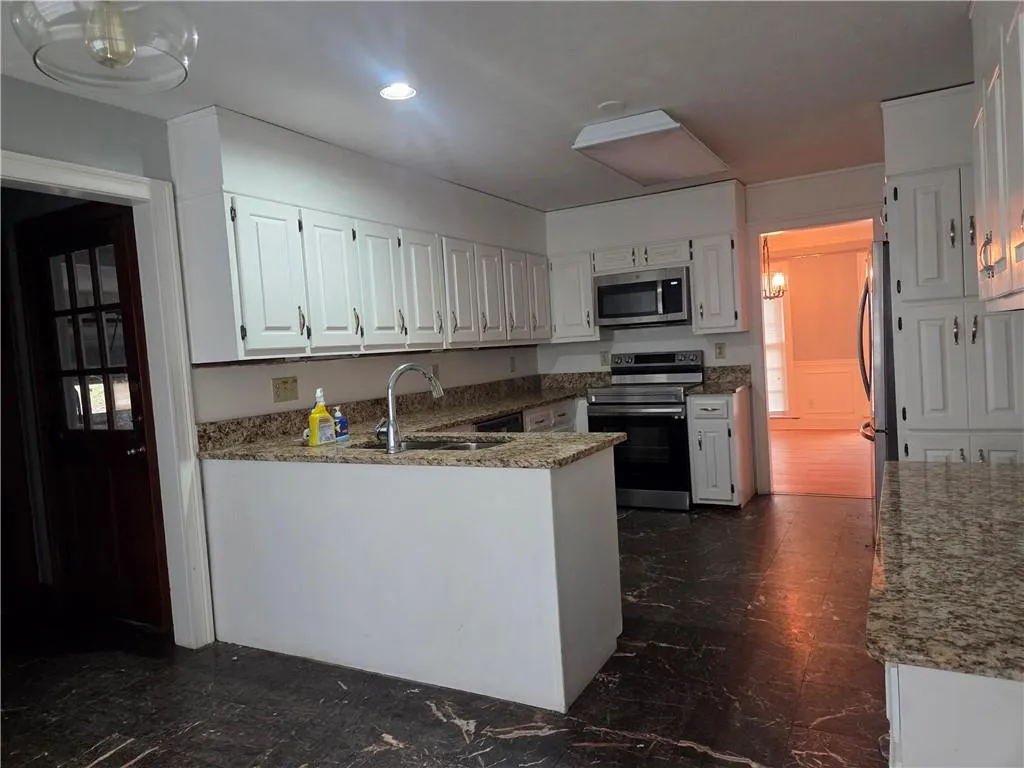 Kitchen featuring appliances with stainless steel finishes, white cabinetry, light stone countertops, a peninsula, and dark marble finish flooring
