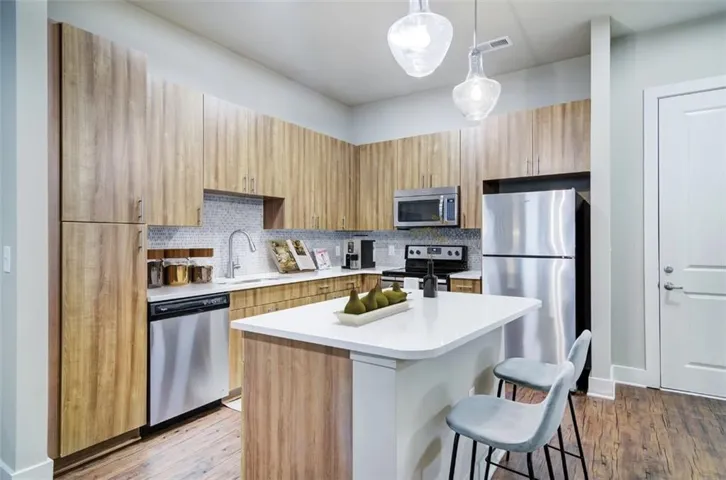 Kitchen with decorative light fixtures, hardwood / wood-style flooring, backsplash, and appliances with stainless steel finishes