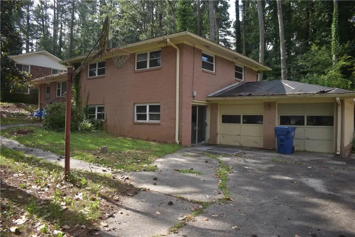 View of front of property with brick siding, driveway, a garage, and view of wooded area