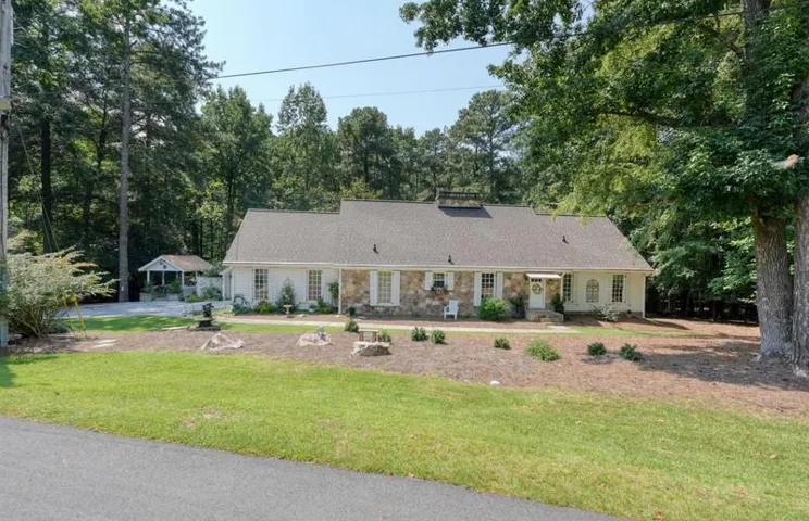 Expansive front lawn with mature trees, stone and siding exterior, shingled roof, white-framed windows, and a detached gazebo structure