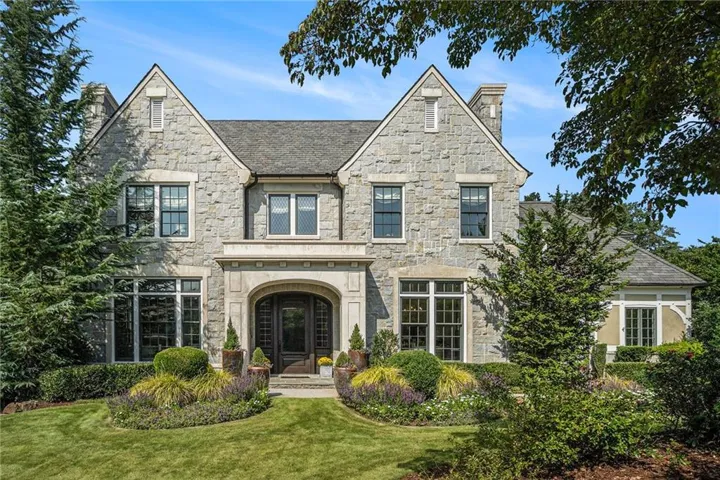 Stone facade residence featuring a prominent arched entry, multiple gabled roofs, and an established front lawn