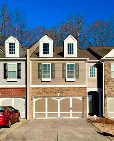 Contemporary townhome exterior featuring a two-car garage with arched panel doors, brick accents, and dormer windows