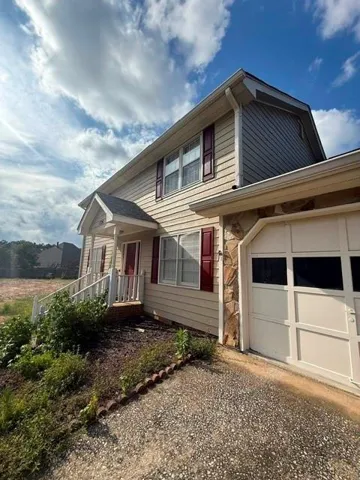 Two-story property featuring light-colored siding with dark red shutters, a prominent front entrance with white railings, and an attached garage with a panel door