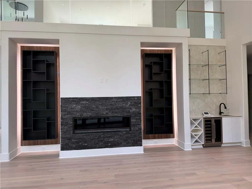 Unfurnished living room with beverage cooler, a glass covered fireplace, light wood-style flooring, and built in shelves Unfurnished living room with beverage cooler, a glass covered fireplace, light wood-style flooring, and built in shelves