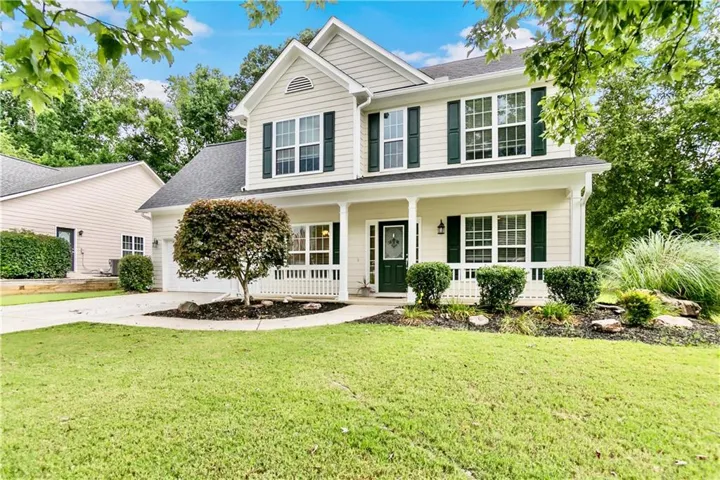 Two-story residence with a covered front porch featuring white railings, an attached two-car garage, and a dark green front door