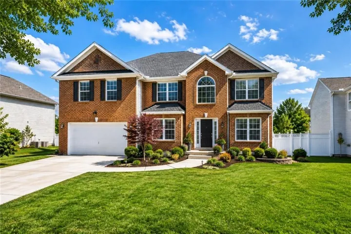 Brick facade residence featuring a two-car garage, manicured landscaping, a prominent arched window, a covered portico entrance, and a white picket fence