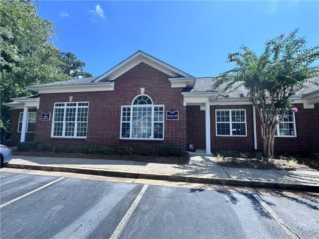 Brick exterior with white trim, multiple large windows, covered entryway, and mature landscaping