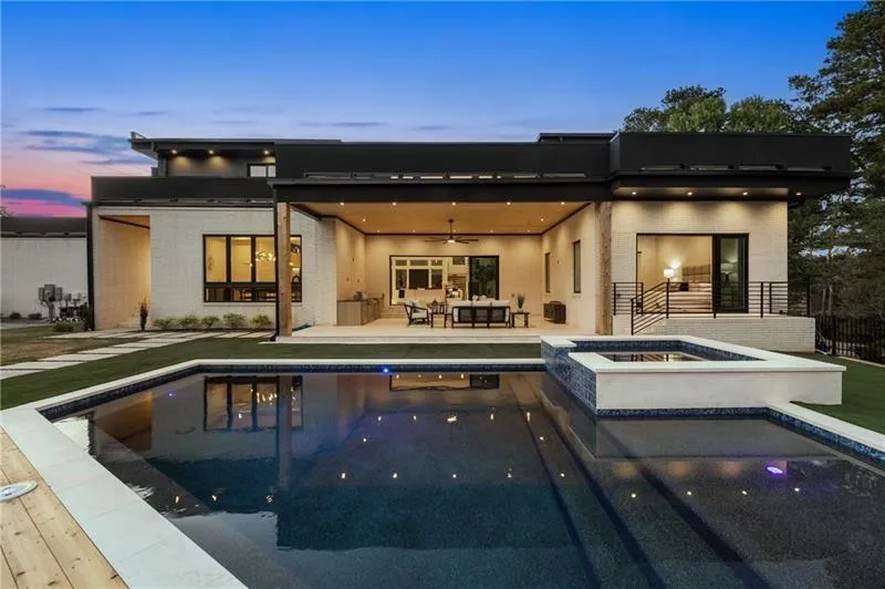 Back of property at dusk with ceiling fan, a patio area, brick siding, and a pool with connected hot tub