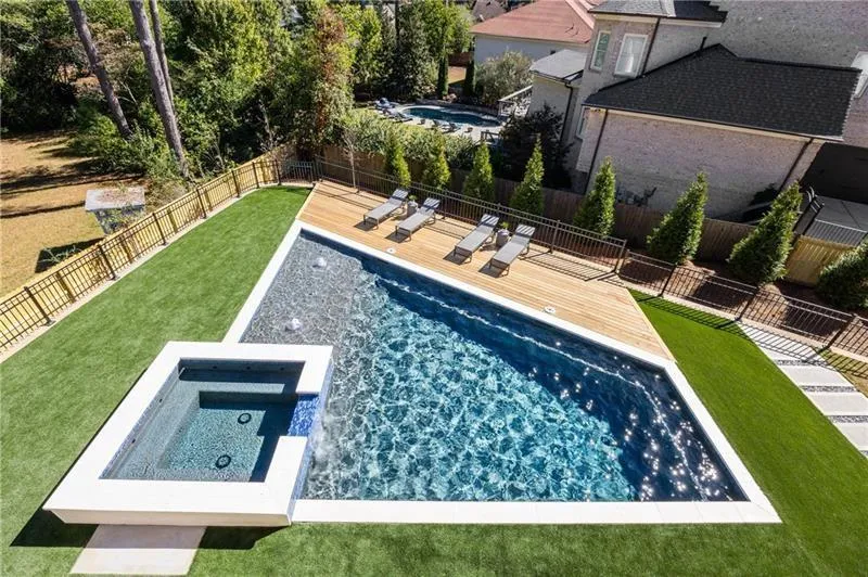 View of swimming pool featuring a deck, a fenced backyard, and a pool with connected hot tub