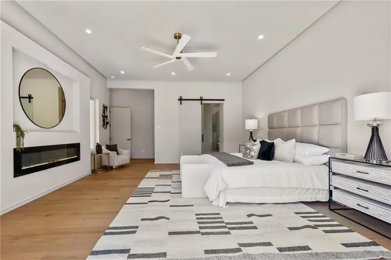 Bedroom featuring a barn door, a glass covered fireplace, light wood-style floors, ceiling fan, and recessed lighting