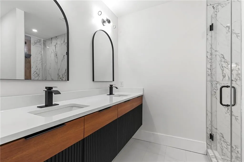 Full bathroom featuring double vanity, a marble finish shower, and light tile patterned floors