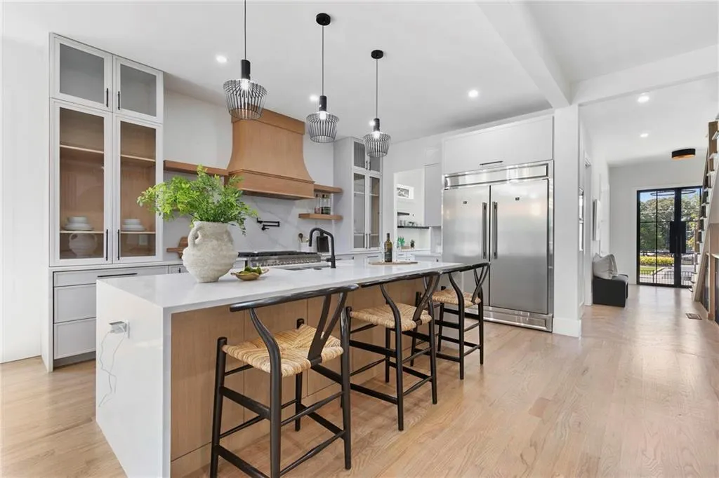 Kitchen with a kitchen breakfast bar, white cabinets, hanging light fixtures, built in refrigerator, and a kitchen island with sink