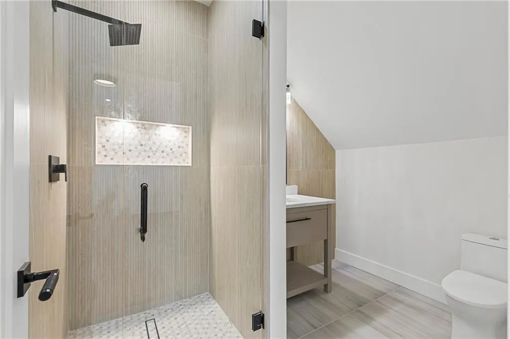 Bathroom featuring a stall shower, vanity, vaulted ceiling, and light tile patterned floors
