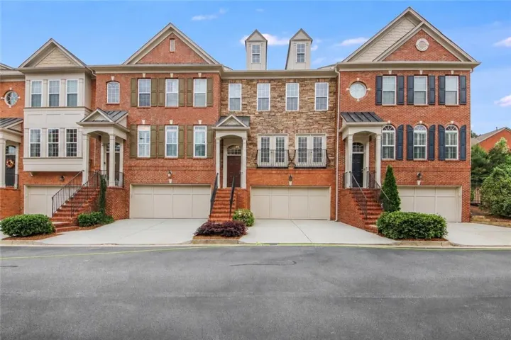 Brick exterior townhome featuring a stone facade accent, dormer windows, and a two-car garage