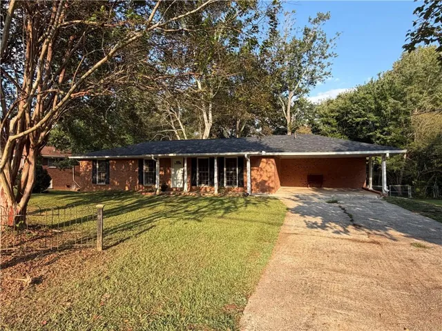 Brick exterior, covered carport, concrete driveway, mature trees, and a front lawn