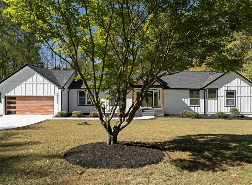 Modern farmhouse style home featuring a front yard, board and batten siding, roof with shingles, and driveway