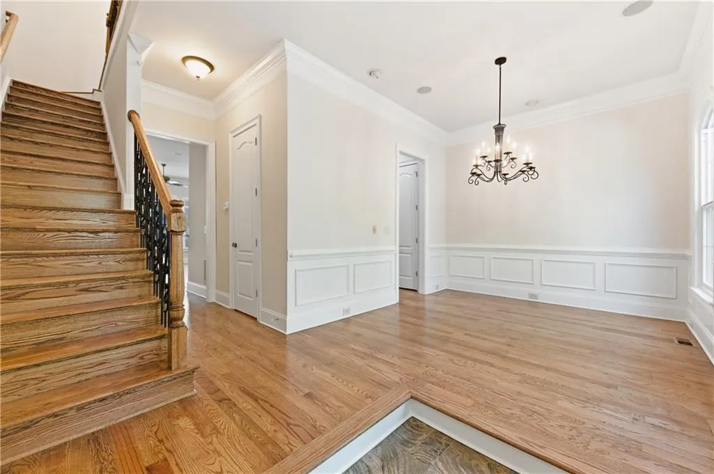 Unfurnished dining area featuring a wainscoted wall, a decorative wall, a chandelier, crown molding, and light wood-type flooring