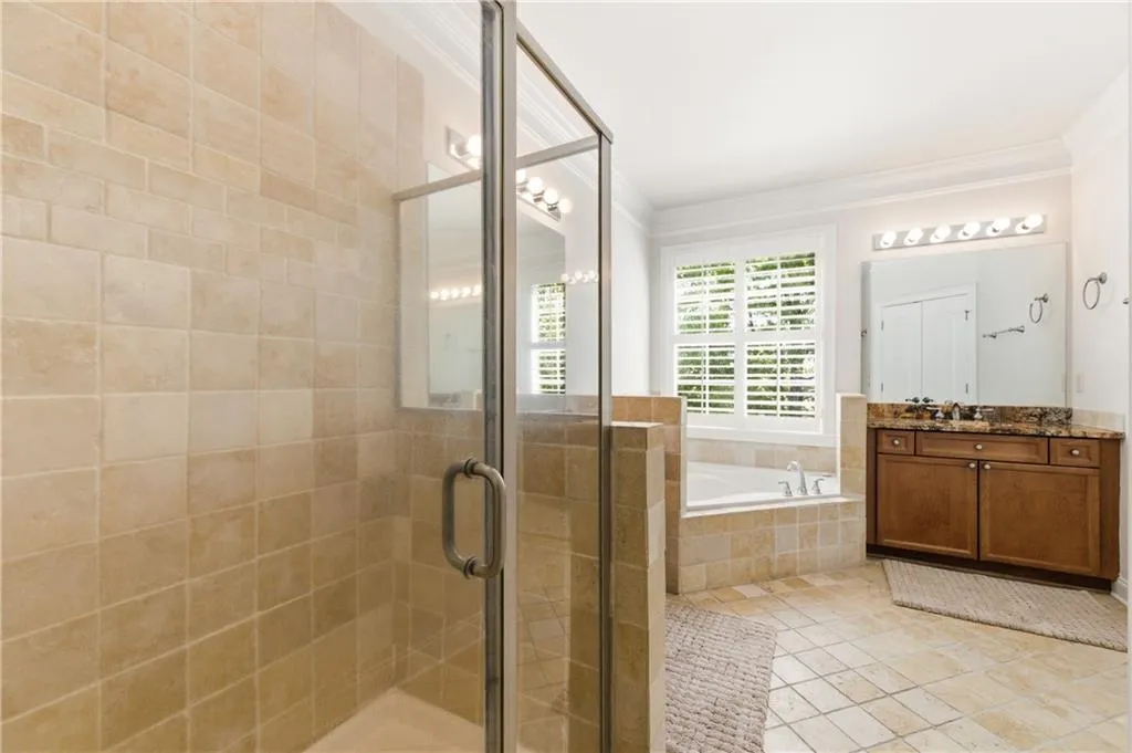 Bathroom featuring vanity, a garden tub, a shower stall, crown molding, and light tile patterned floors